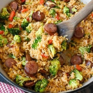 A wooden spoon scooping up some sausage rice skillet.