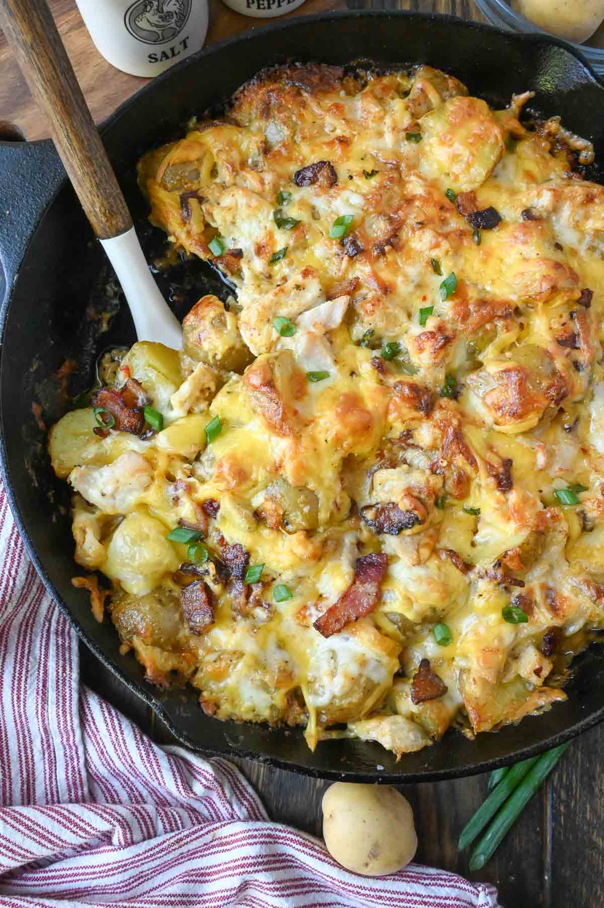 A spoon in a skillet with cheesy potato bake.