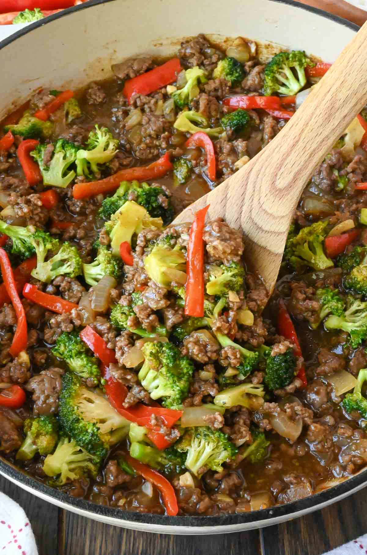 Stirring ground beef broccoli skillet with a wooden spoon.