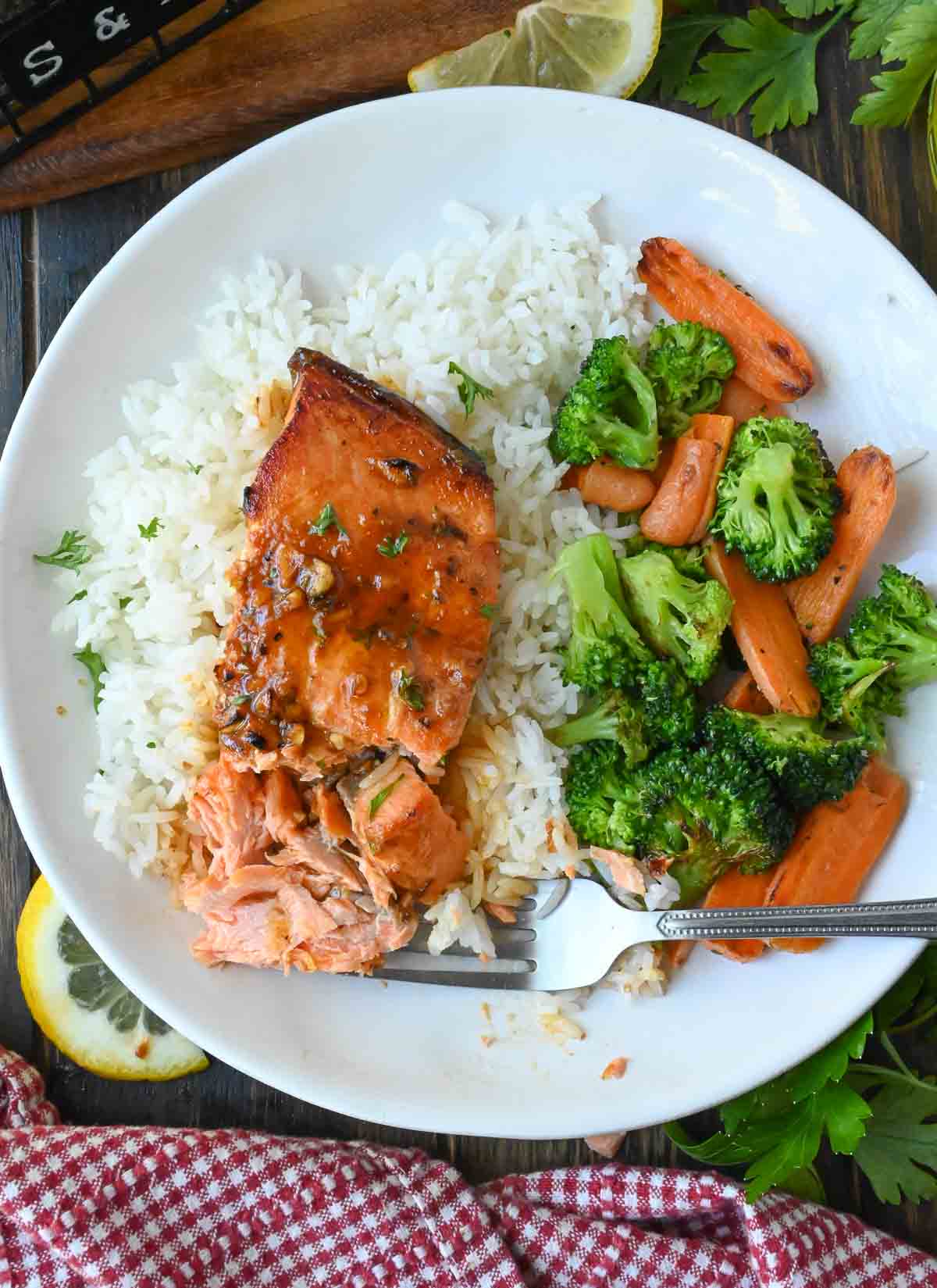 A plate of baked steelhead trout served over rice with broccoli and carrots.