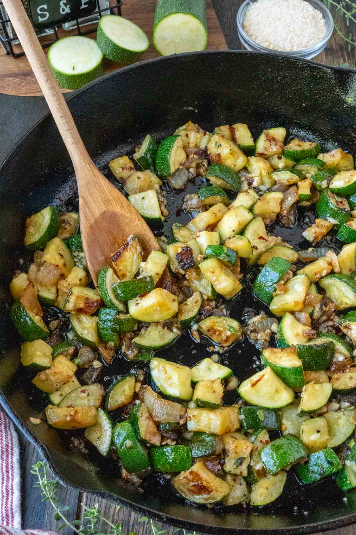 Stirring zucchini and onions in a skillet with a wooden spoon.