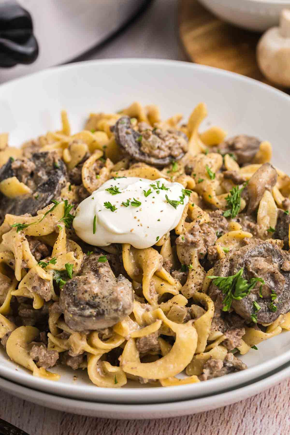 A bowl of ground beef slow cooker stroganoff with sour cream and fresh herbs.