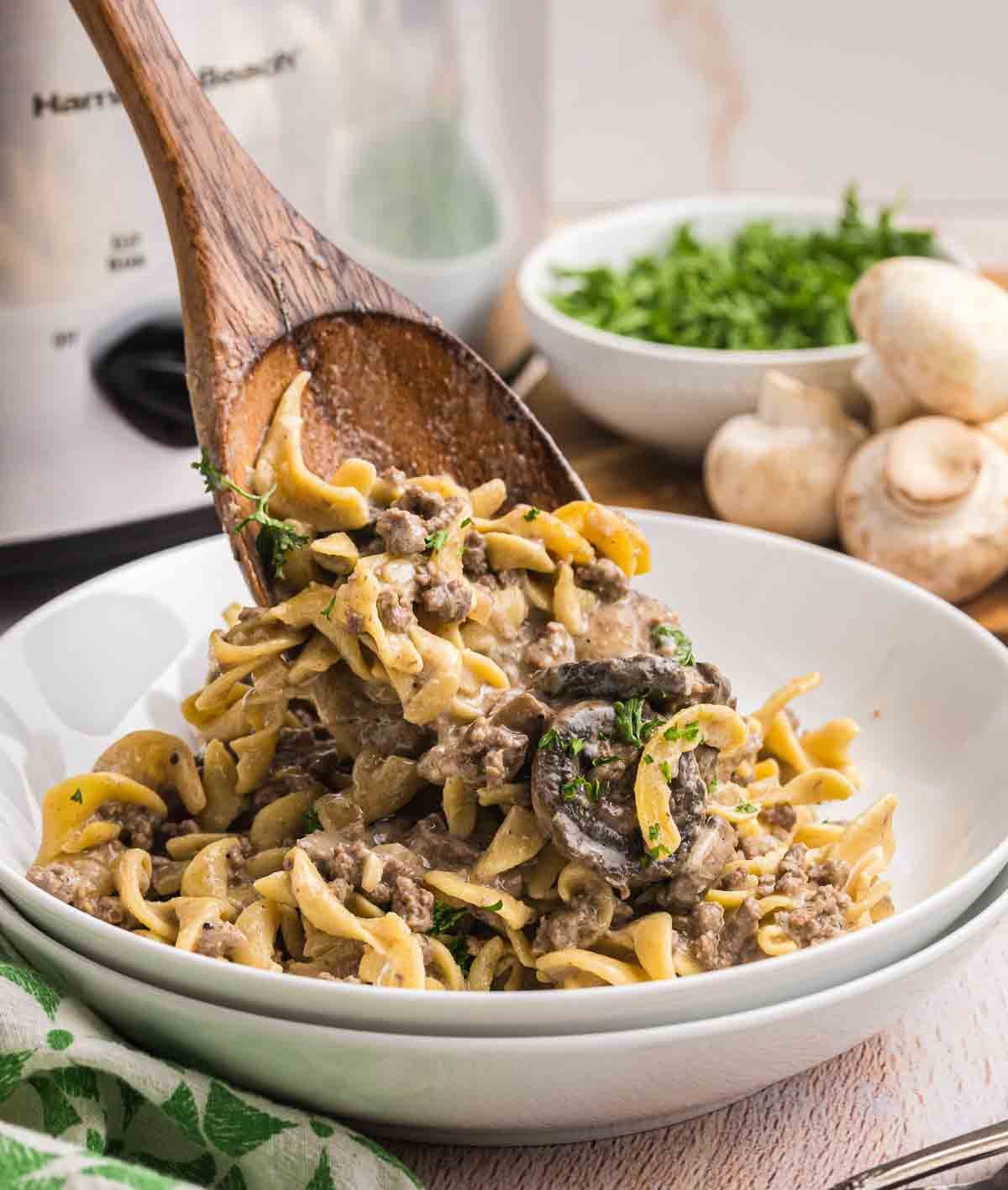 Spooning ground beef slow cooker stroganoff into a white bowl.