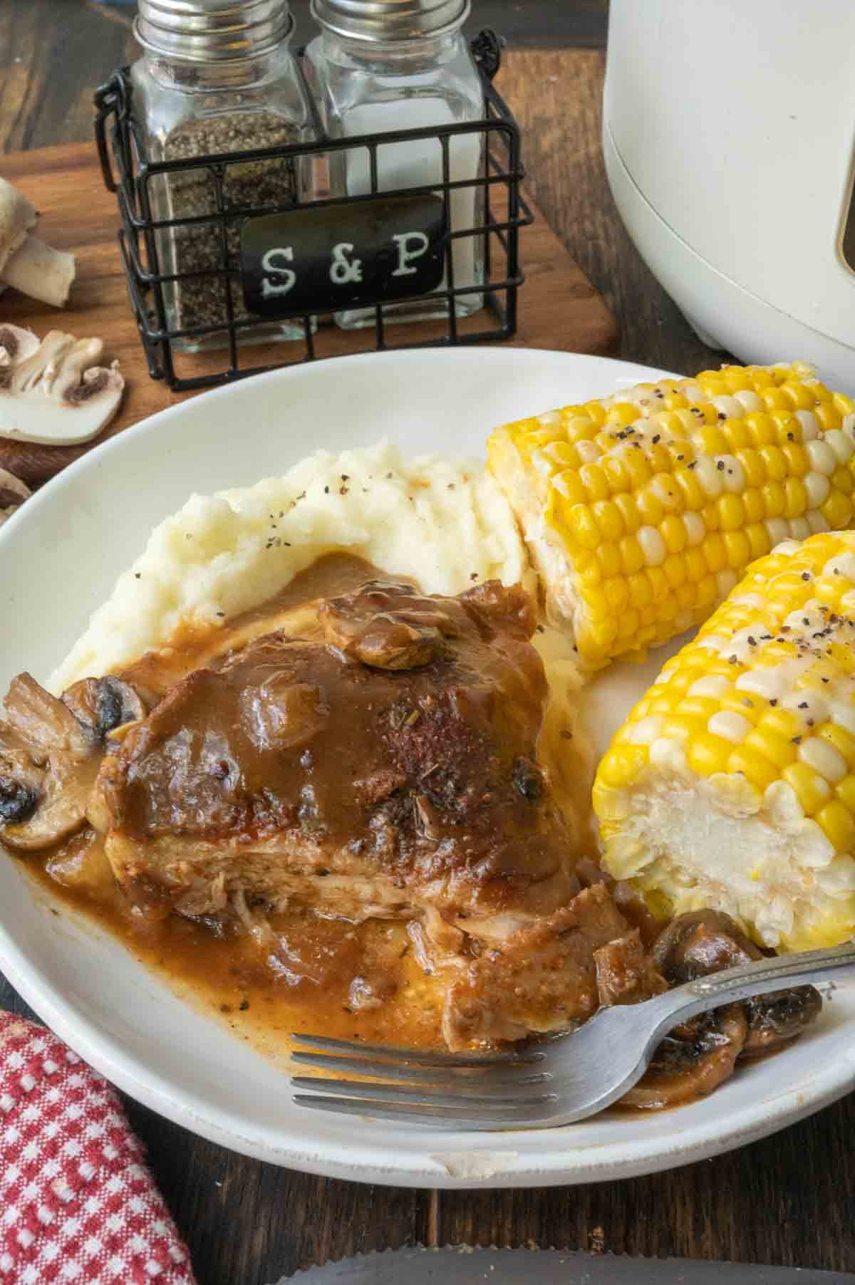 A plate of smothered chicken with potatoes and corn on the cob.