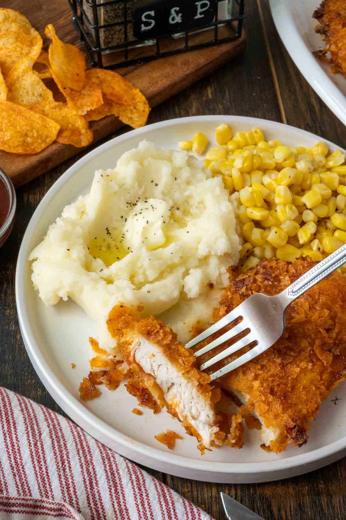 A plate of potato chip chicken with mashed potatoes and corn.