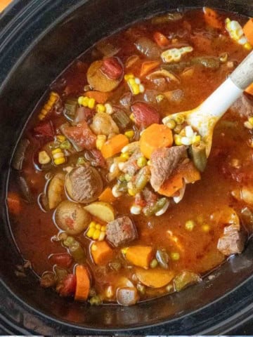 A wooden spoon scooping out some vegetable beef broth soup.