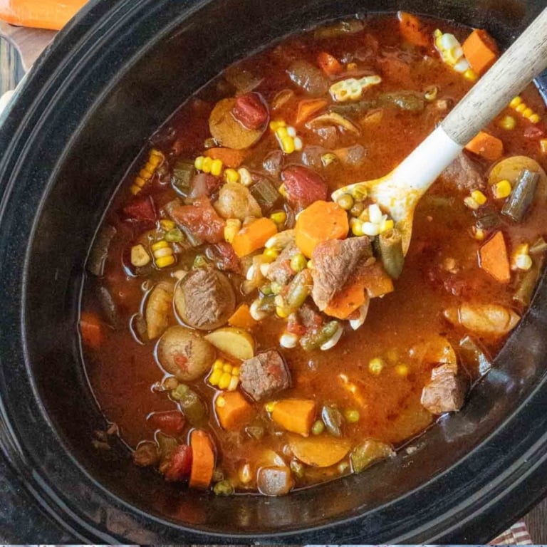 A wooden spoon scooping out some vegetable beef broth soup.