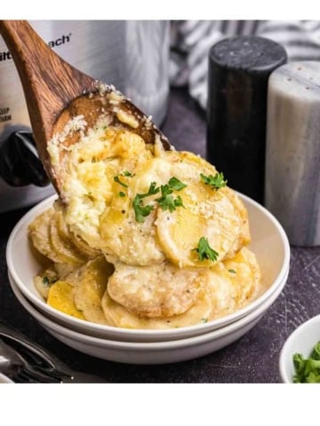 Spooning scalloped potatoes into a dish.