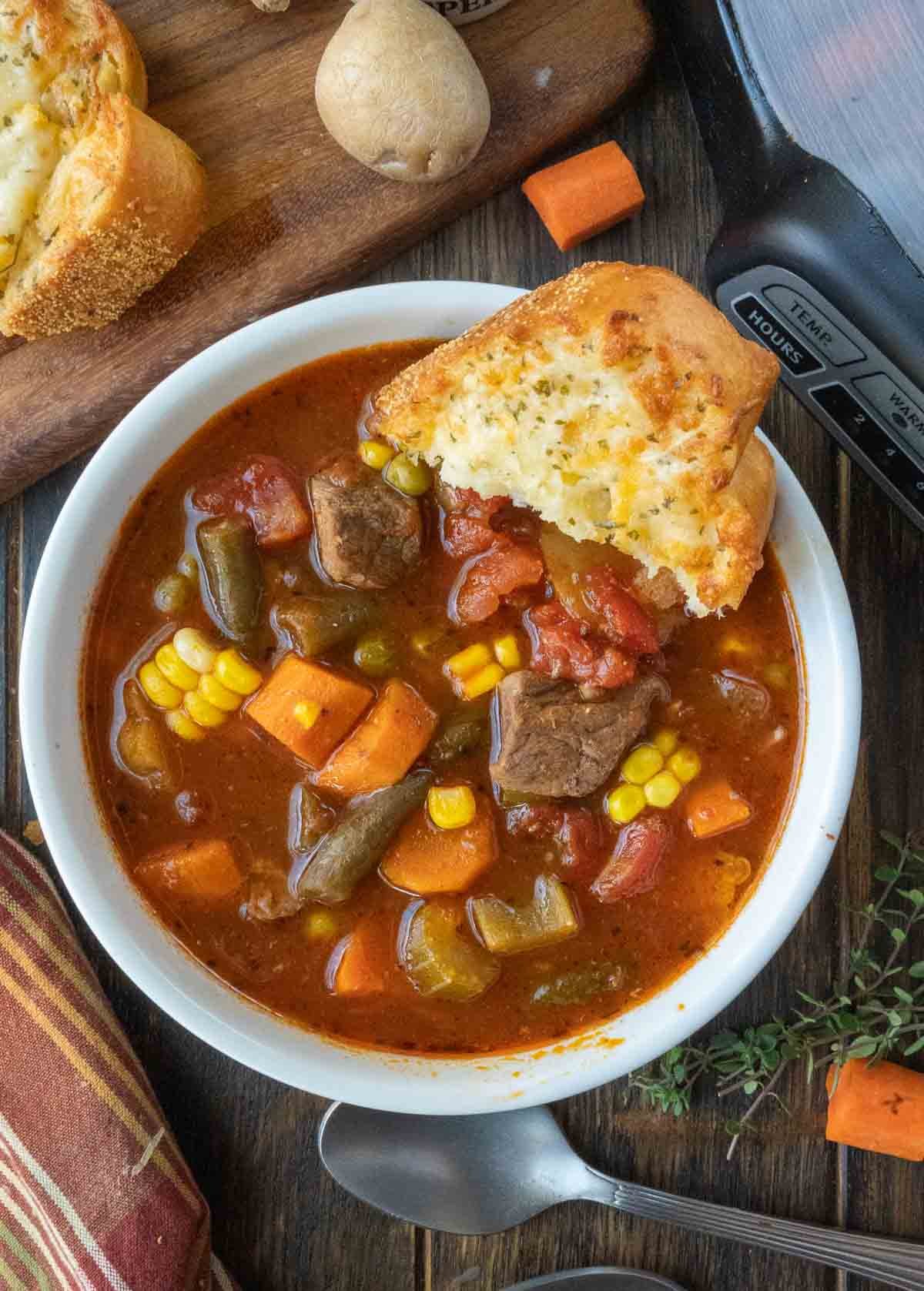 A bowl of vegetable beef soup with crusty bread.