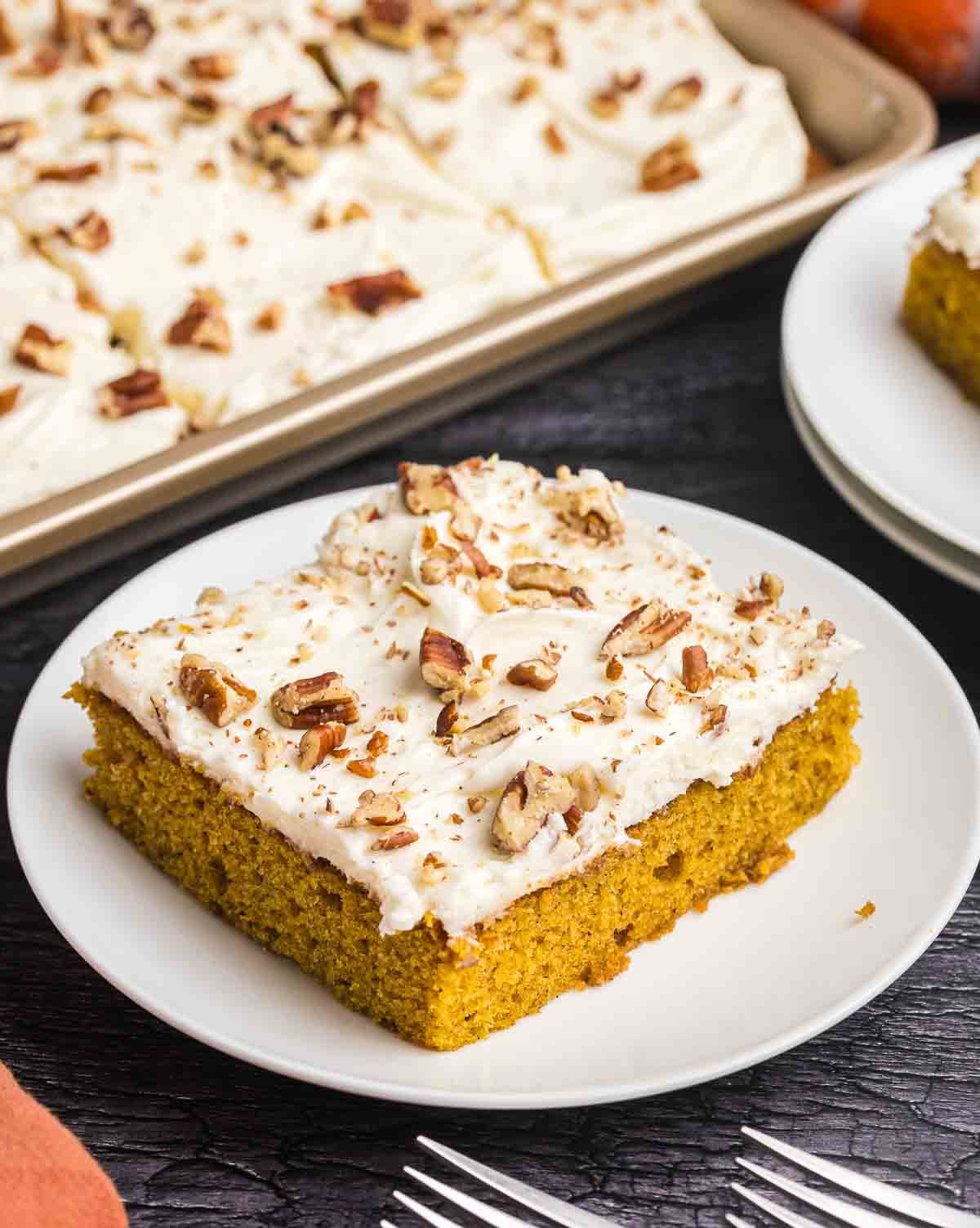 A plate of pumpkin sheet cake with a full sheet pan of cake in the background.
