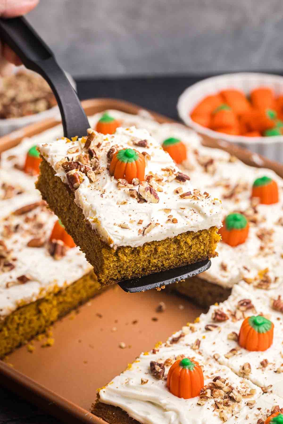 Lifting up a decorated slice of pumpkin sheet cake.