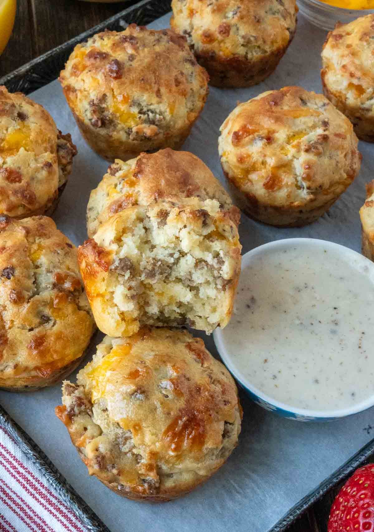 A tray of sausage muffins with gravy, one with a bit taken out of it.