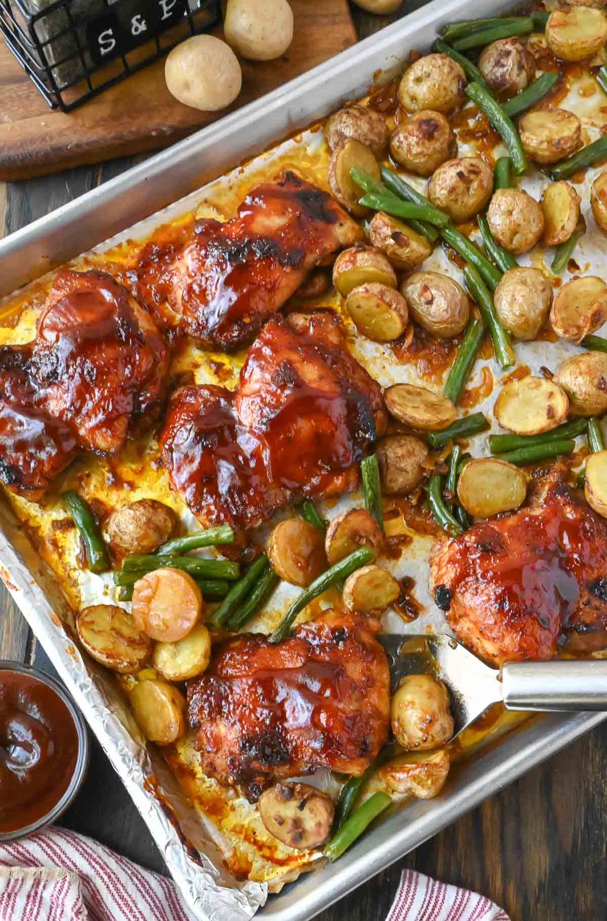A sheet pan with bbq baked chicken potatoes and green beans.
