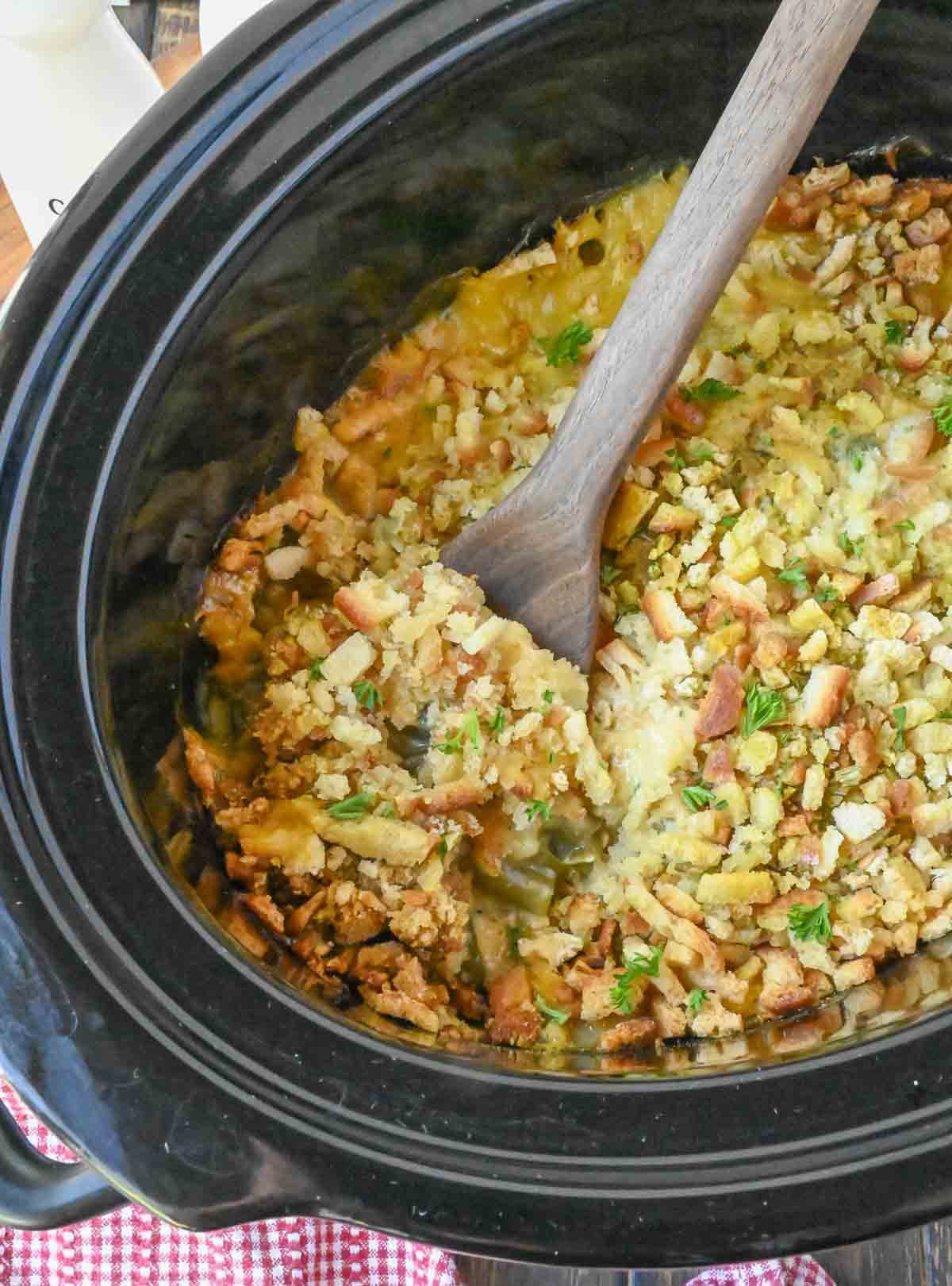 A wooden spoon in a slow cooker with chicken stuffing casserole.