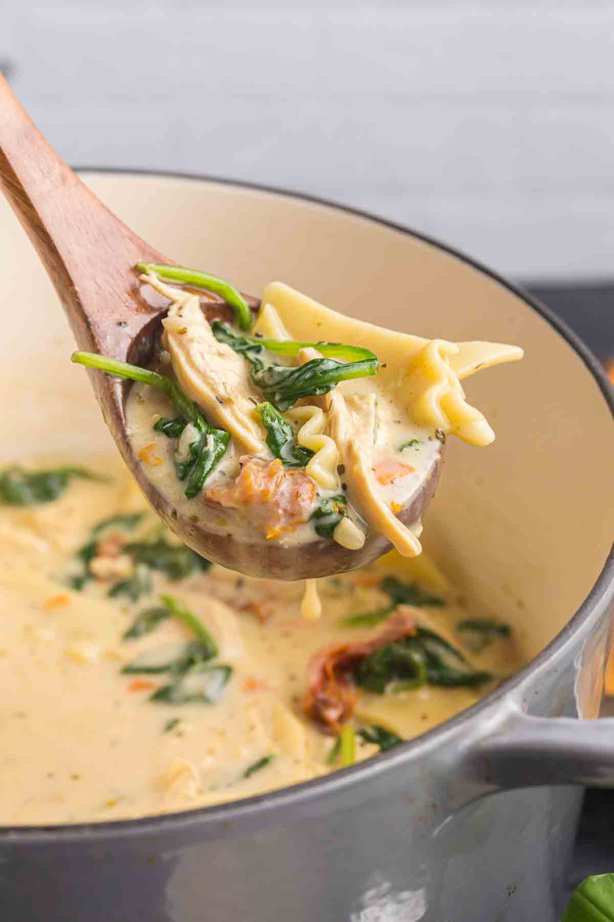 Scooping up white lasagna soup from a pot.