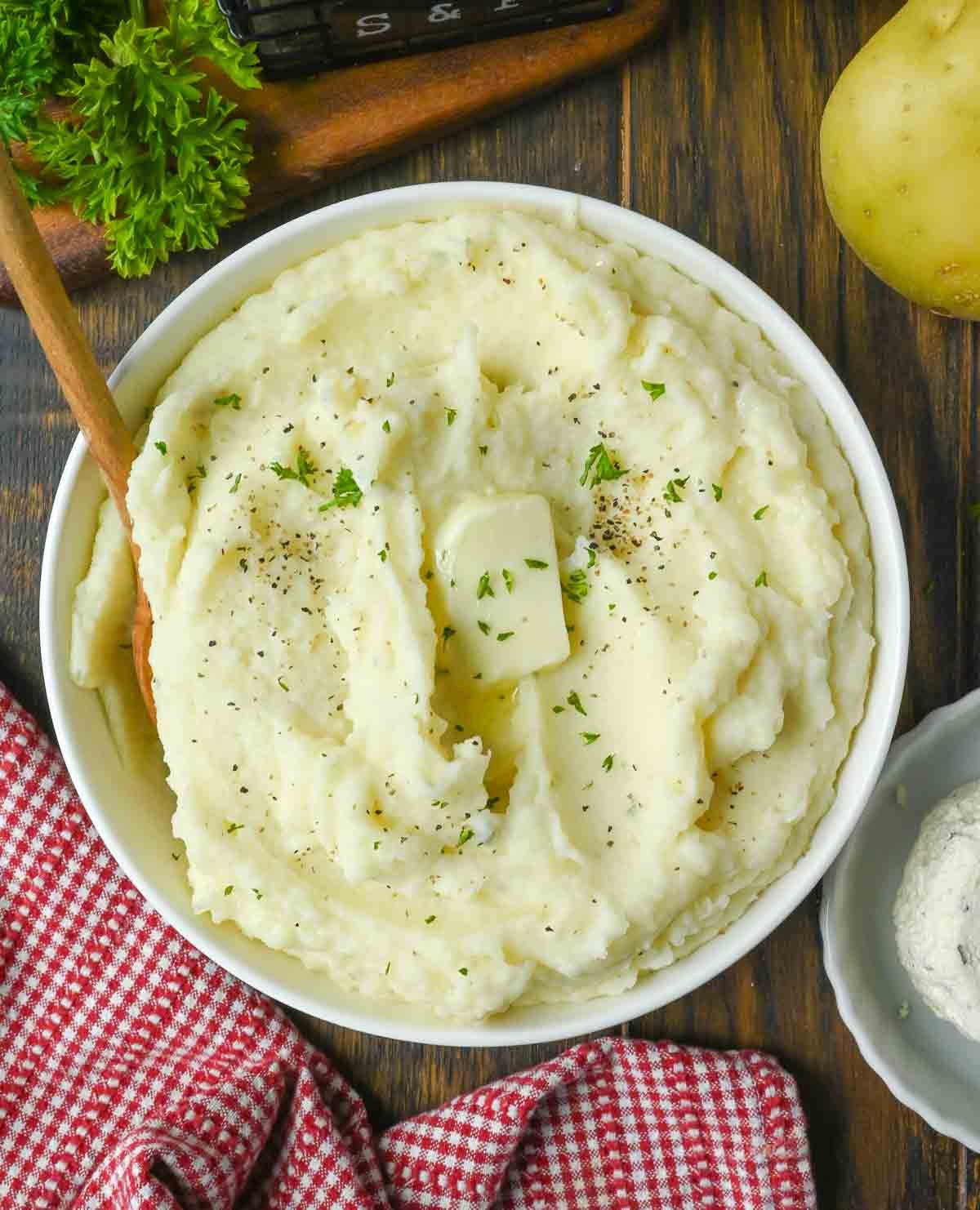 A bowl of Boursin mashed potatoes with a pat of butter and fresh herbs.