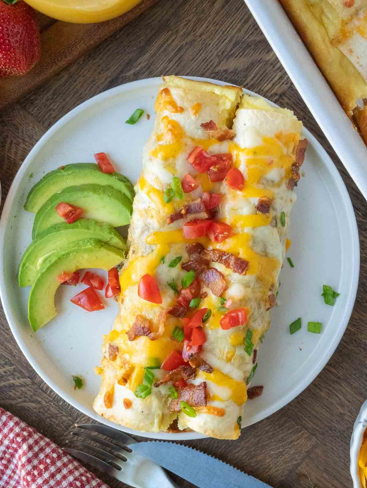 Two breakfast enchiladas on a plate with avocado garnish.