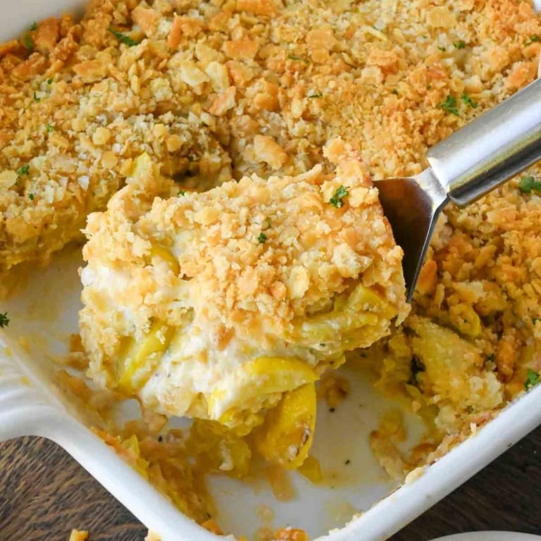 Taking a scoop of cheesy squash casserole from a baking dish.