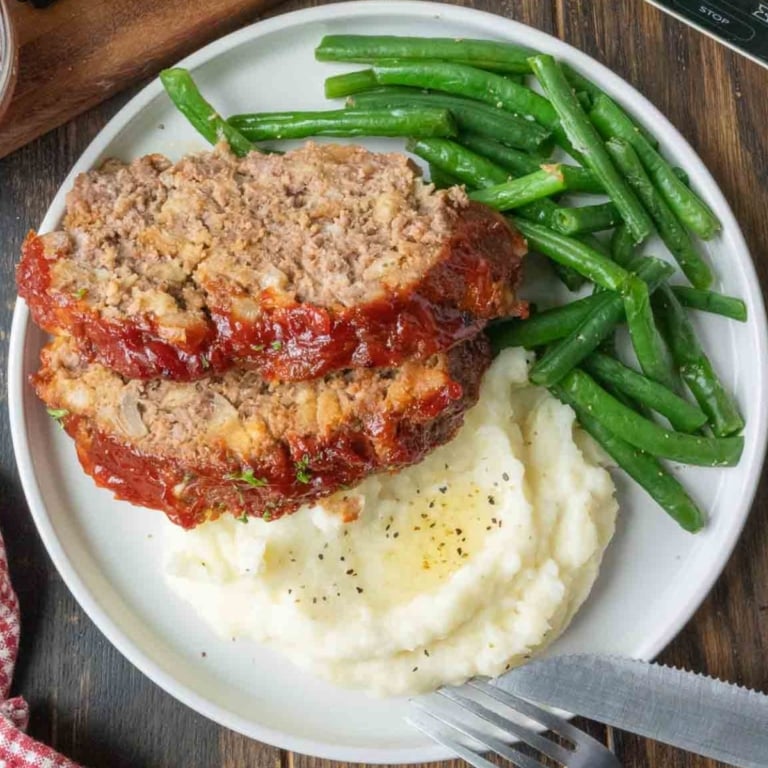 Slow cooker meatloaf on a plate with mashed potatoes and green beans.