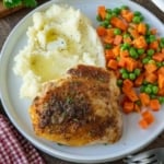 A plate of crispy roasted chicken with mashed potatoes and vegetables.