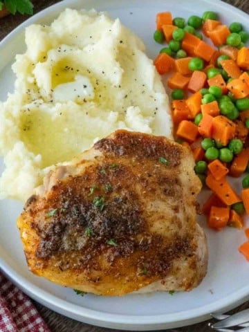 A plate of crispy roasted chicken with mashed potatoes and vegetables.