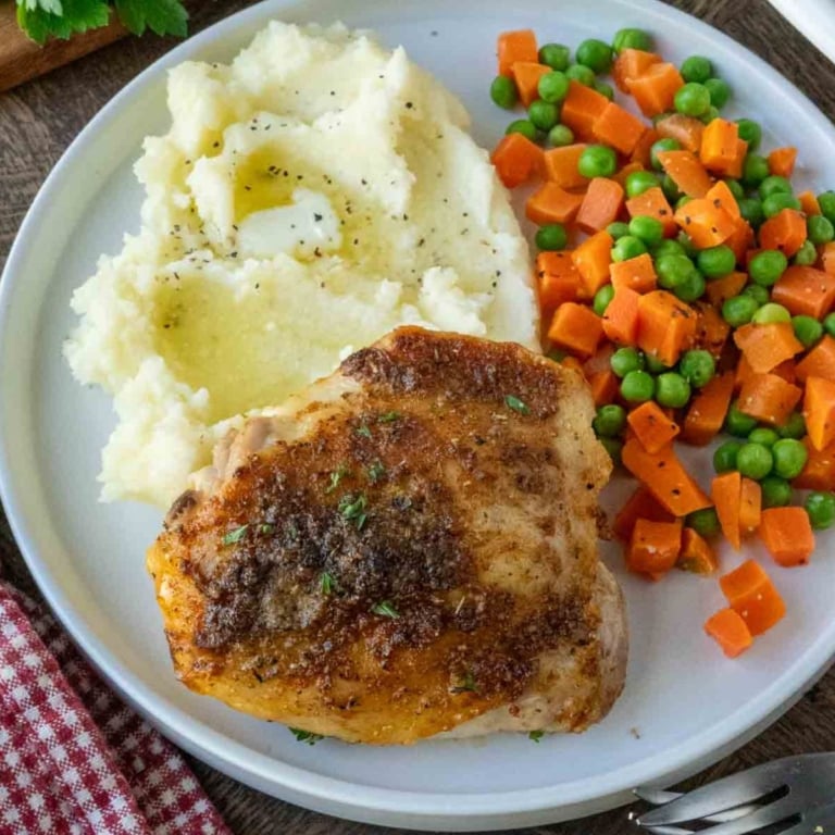 A plate of crispy roasted chicken with mashed potatoes and vegetables.