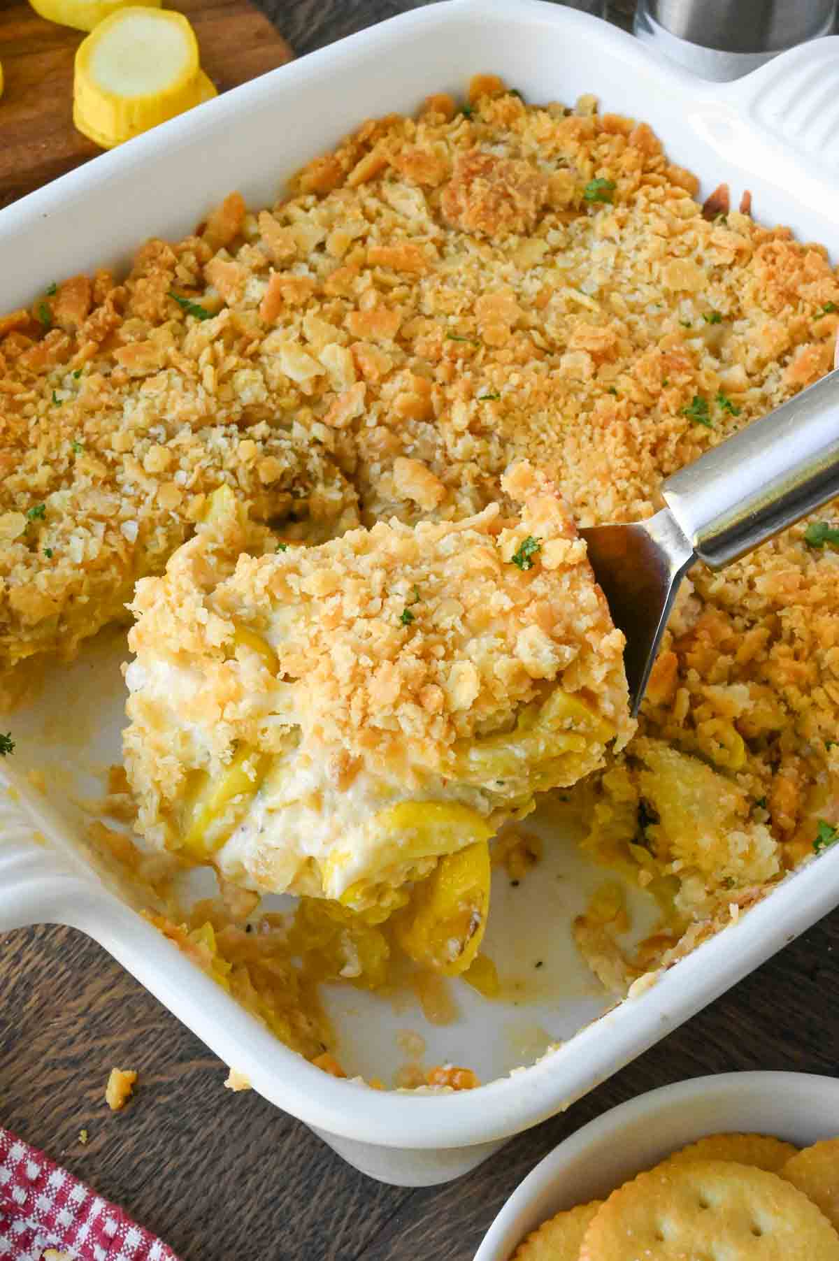 Taking a scoop of cheesy squash casserole from a baking dish.