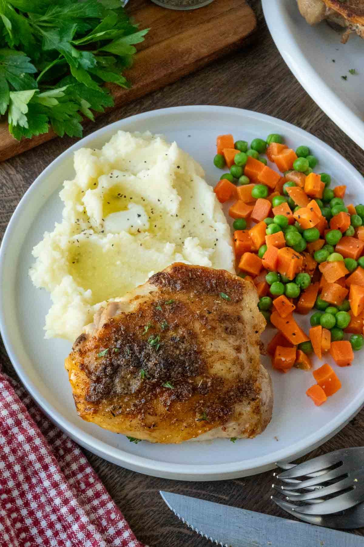 A plate of crispy roasted chicken with potatoes and peas and carrots.