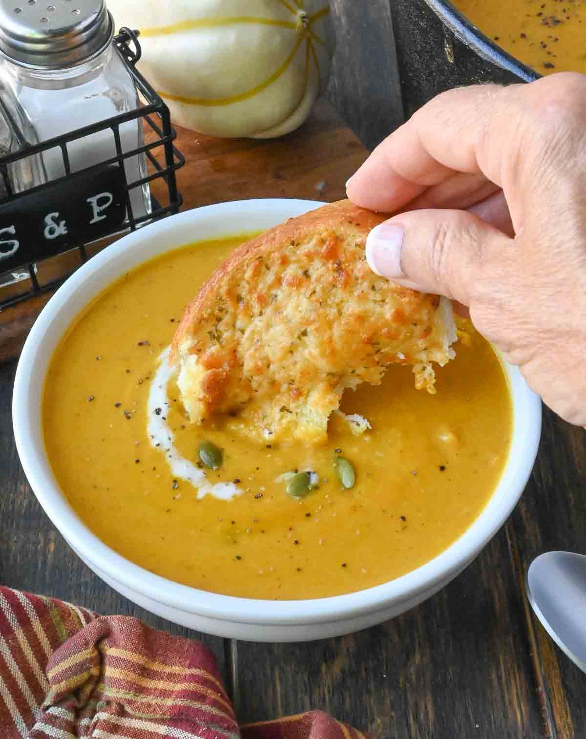 Dipping a piece of bread into a bowl of butternut squash soup.