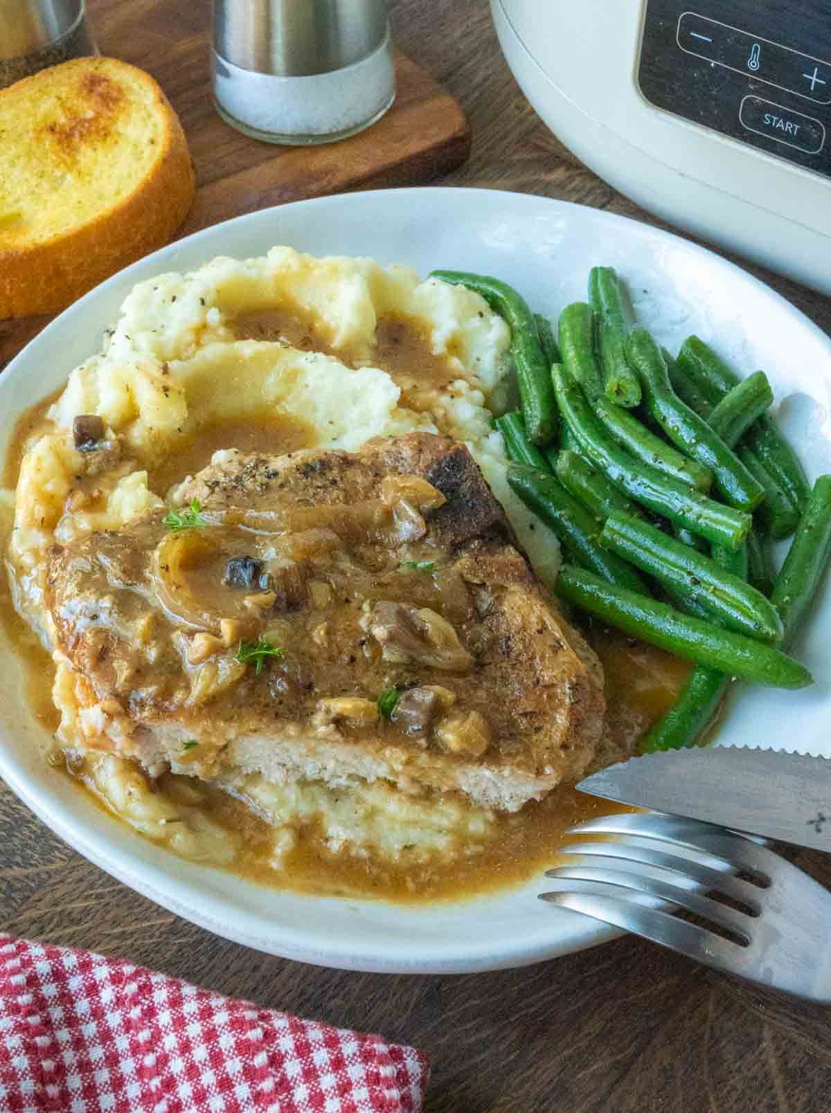Smothered pork chop on a plate with mashed potatoes and green beans.