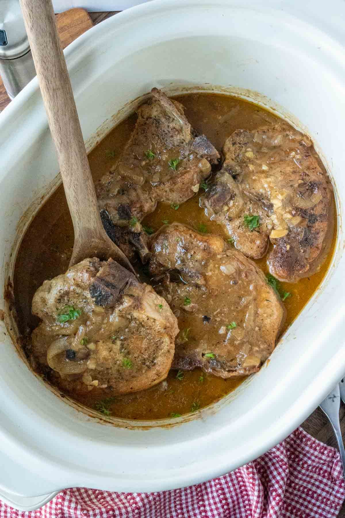 A wooden spatula picking up a pork chop smothered in gravy.