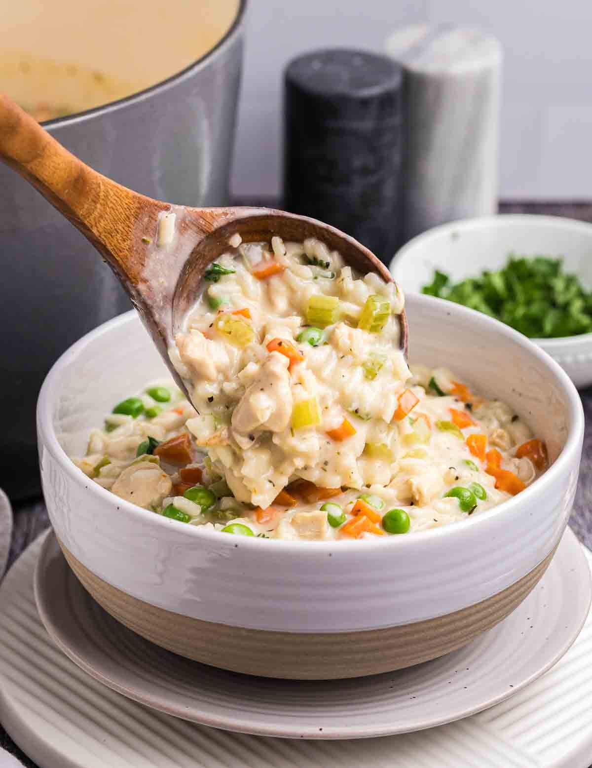 Spooning creamy chicken and rice soup into a bowl.