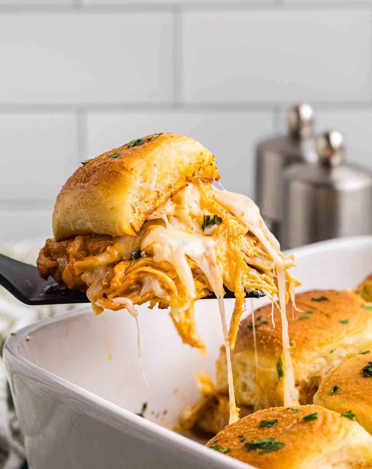 Lifting a melty buffalo chicken slider from a baking dish.