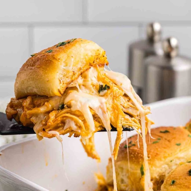 Using a spatula to lift a buffalo chicken slider from a baking dish.