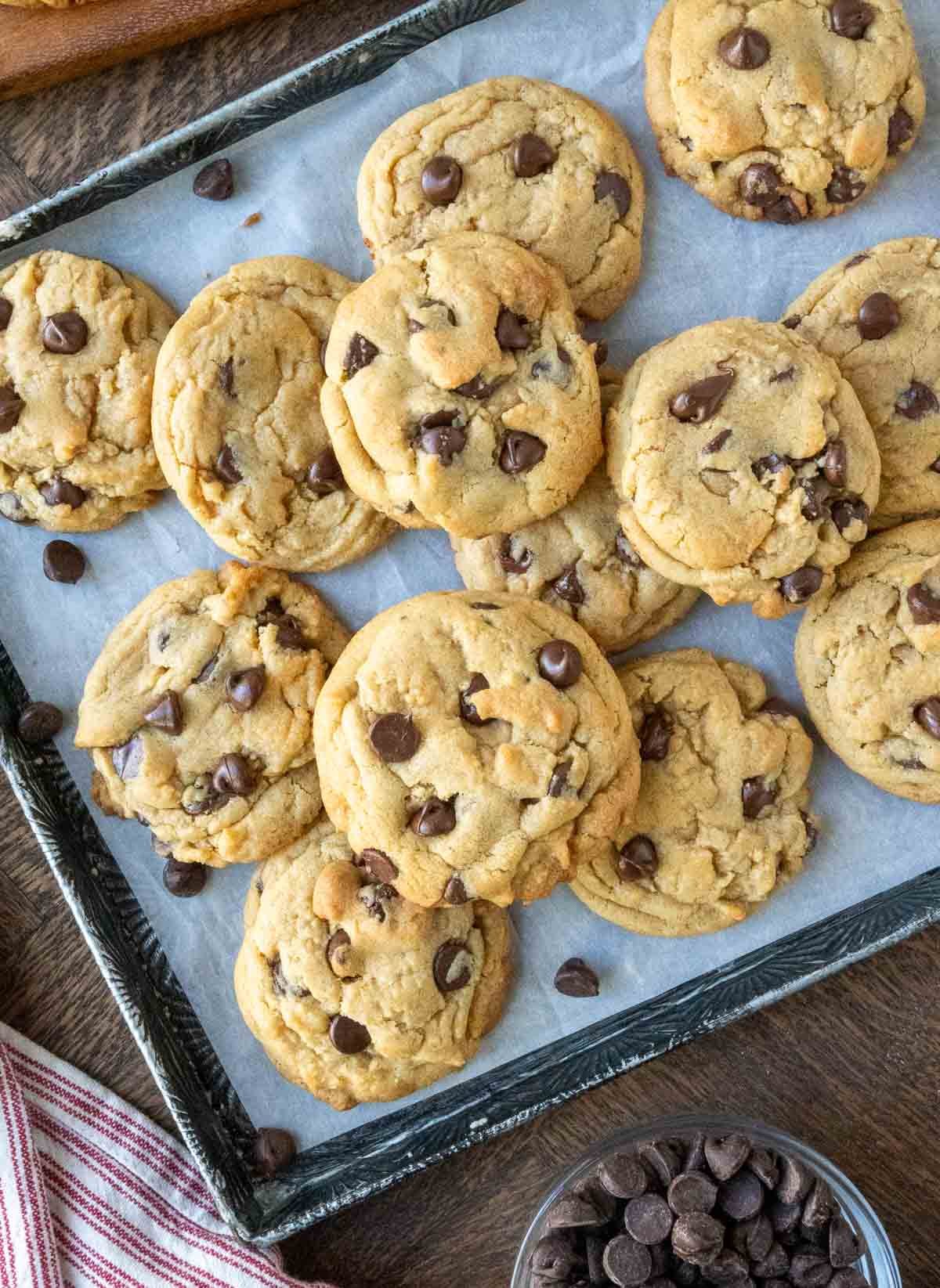 Chocolate chip cookies on a baking sheet with loose chocolate chips.