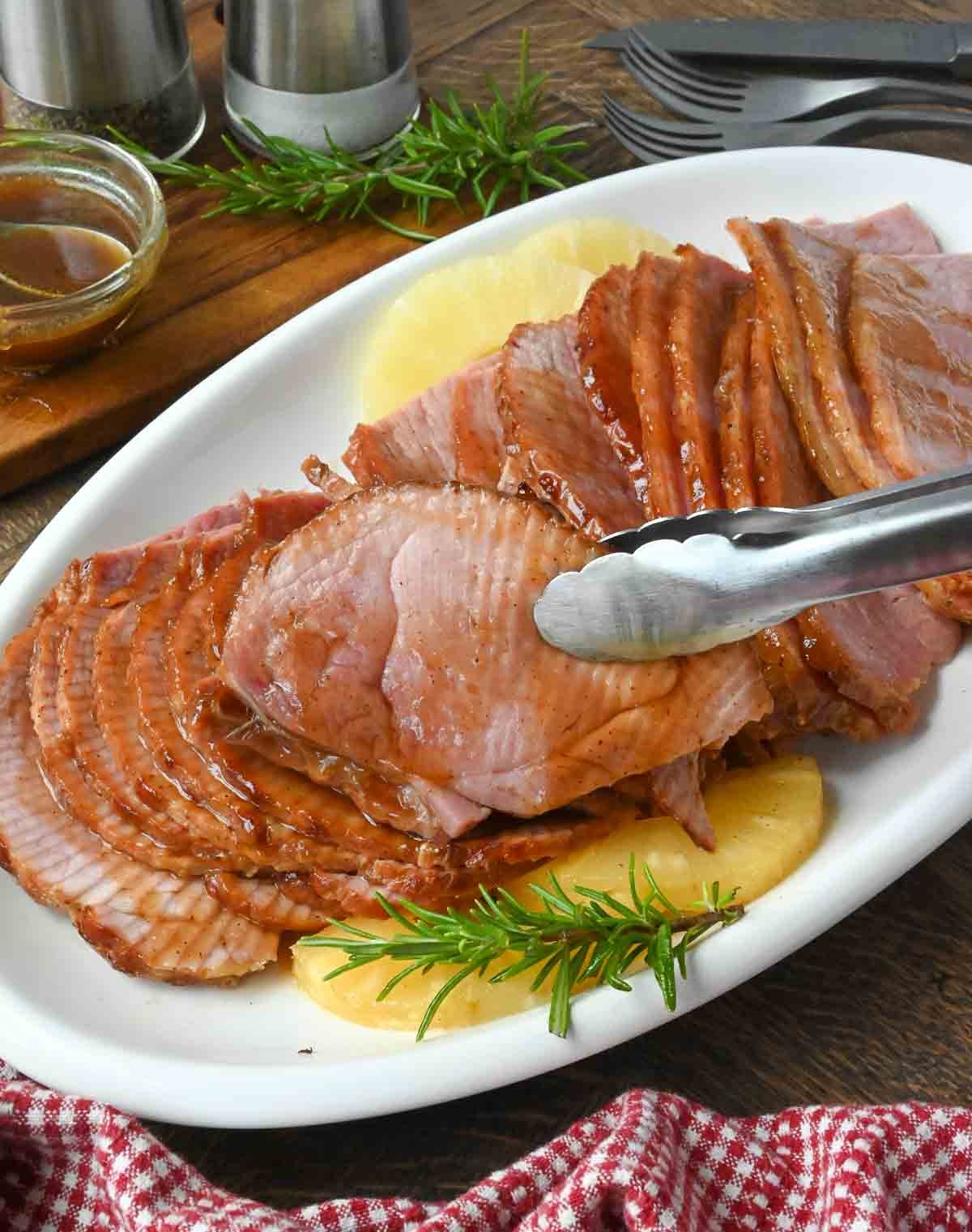 Tongs picking up a slice of pineapple ham.
