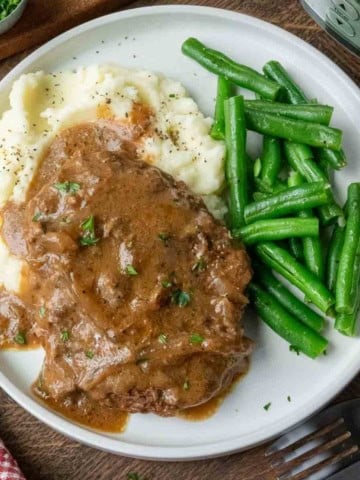 A plate of slow cooker cube steak with potatoes and green beans.