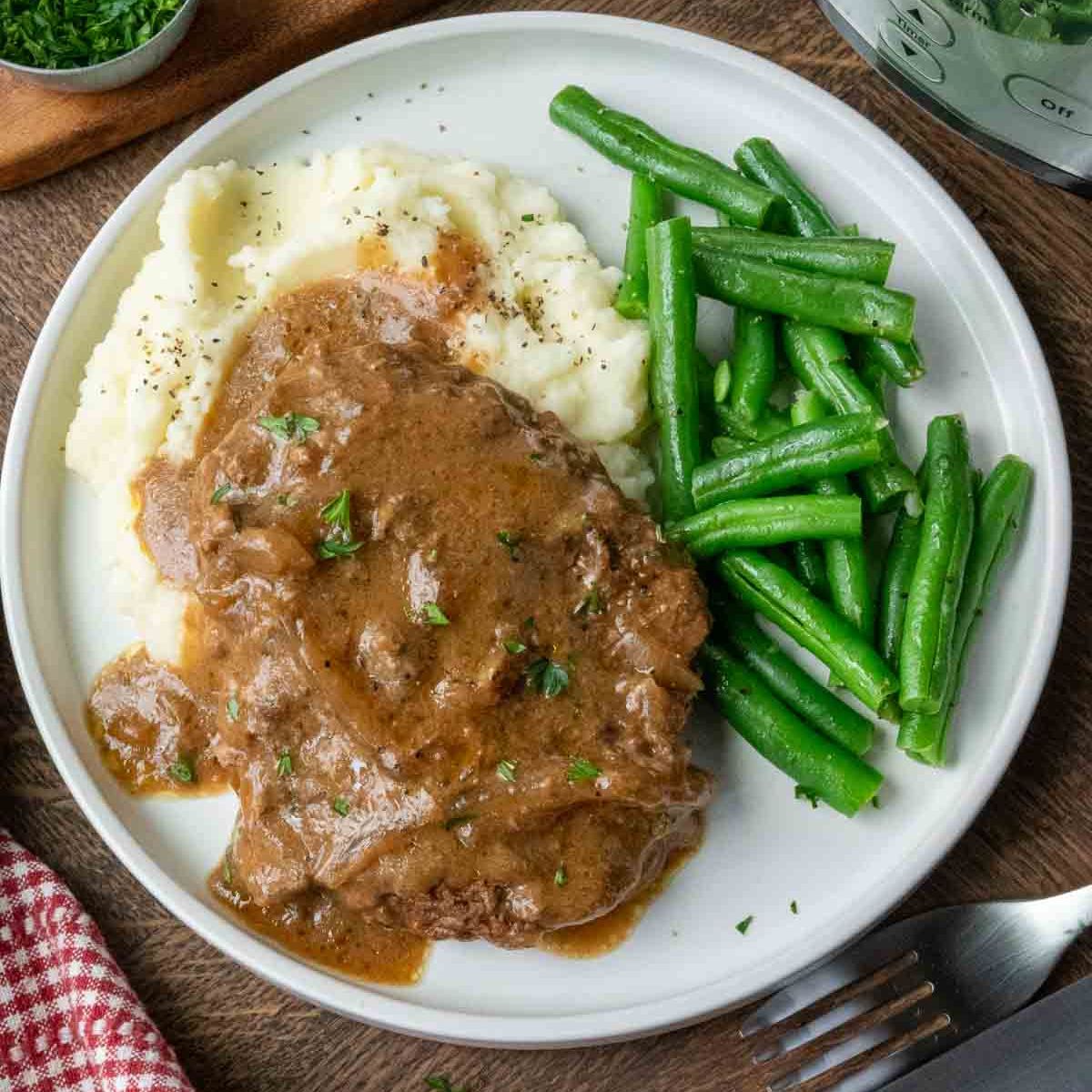 A plate of slow cooker cube steak with potatoes and green beans.
