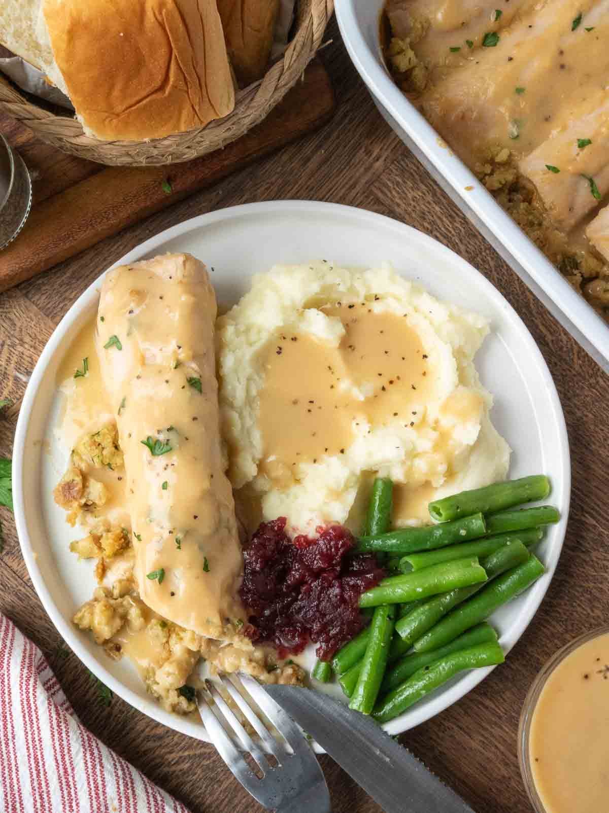 A plate of turkey stuffing roll ups with potatoes and green beans.