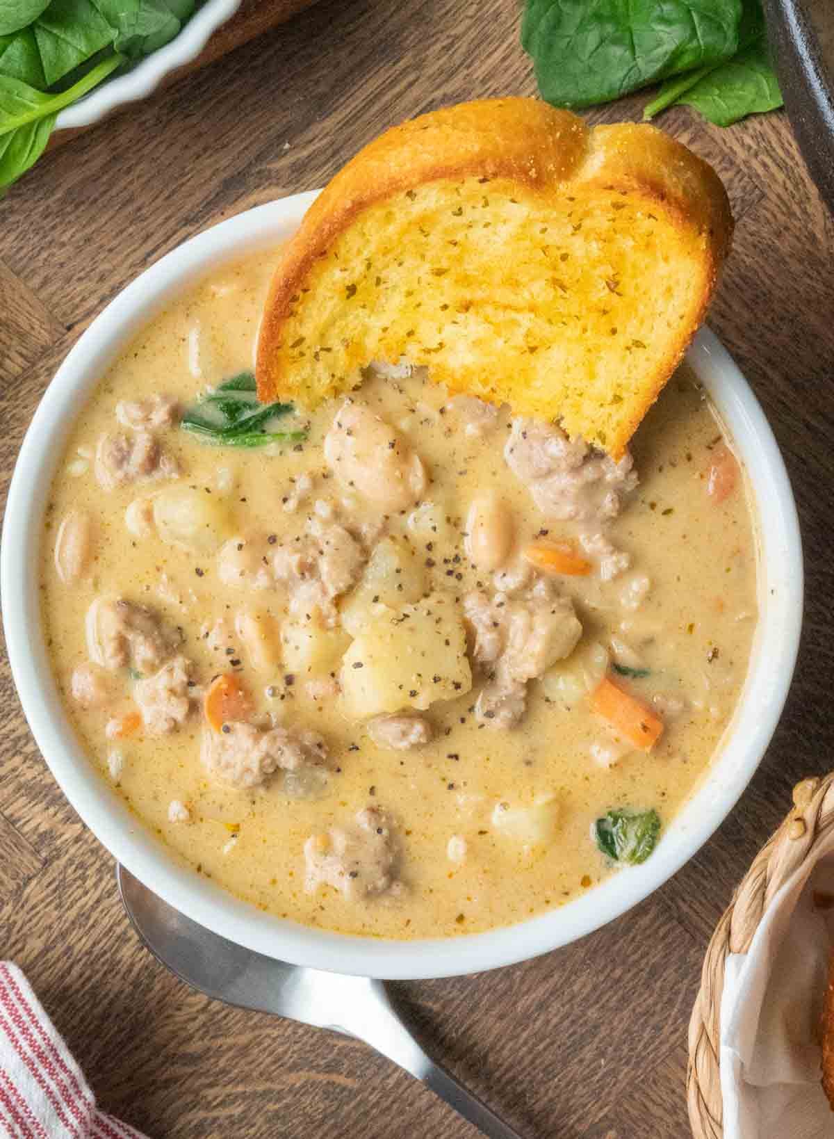 A bowl of Italian sausage white bean soup with a slice of Texas toast.