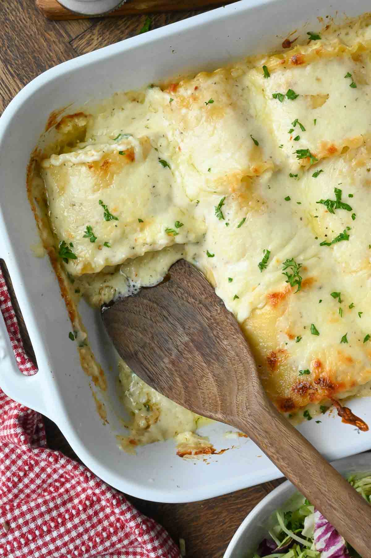 A wooden spatula in a baking dish with lasagna roll ups.