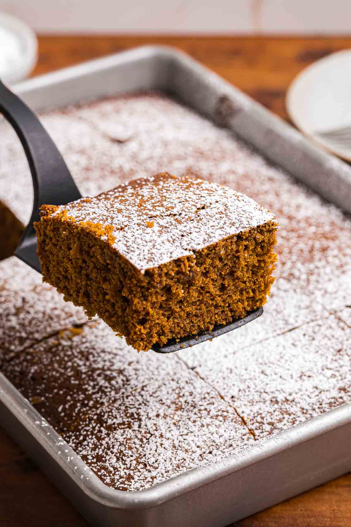 Lifting a piece of gingerbread cake out of a silver baking pan.