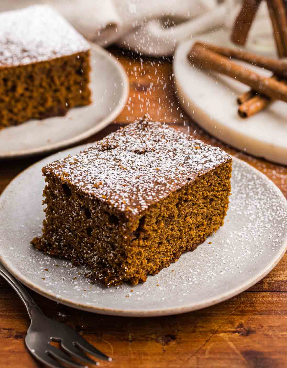 Sprinkling powdered sugar over a slice of gingerbread cake.