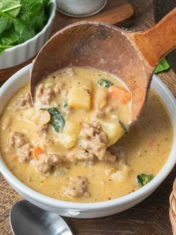 Spooning white bean soup into a bowl with a wooden ladle.