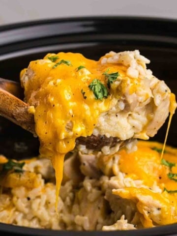 Taking a large scoop of slow cooker chicken and rice with a wooden spoon.