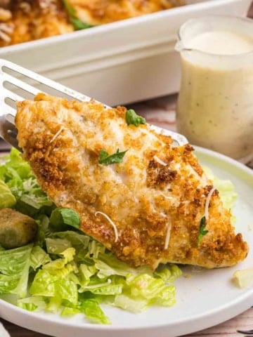 A plate of baked caesar chicken served over salad with croutons.