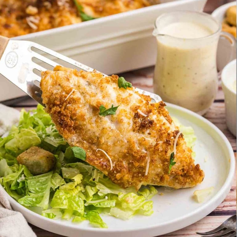 A plate of baked caesar chicken served over salad with croutons.