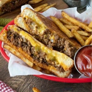Sloppy joe grilled cheese cut in half with a side of fries.