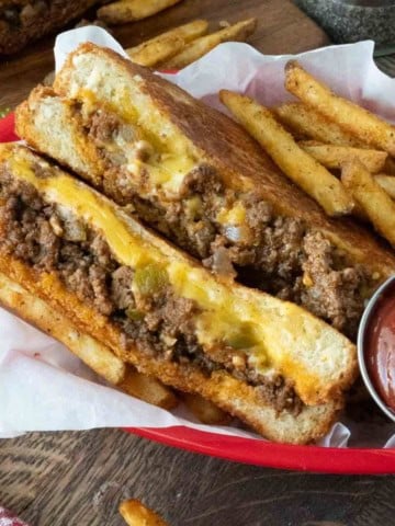Sloppy joe grilled cheese cut in half with a side of fries.