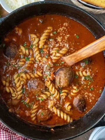 Italian meatball soup with a wooden spoon in a pot.